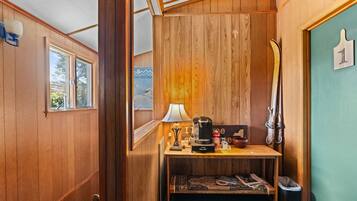 A compact room with wooden walls, a small table with a lamp, a coffee maker, and a ski rack.