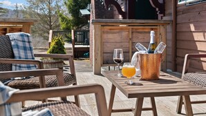 An outdoor seating area with wicker chairs and a wooden table, a bottle of champagne, and a glass of orange juice.