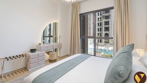 Hotelkamer met een groot bed, een kaptafel met spiegel, een houten rek voor kleding en uitzicht op een zwembad en gebouwen.
