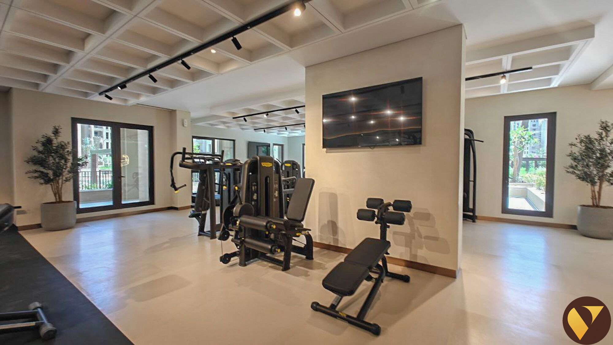 Een ruime fitnessruimte met diverse trainingsapparaten, grote ramen en een modern plafondontwerp.