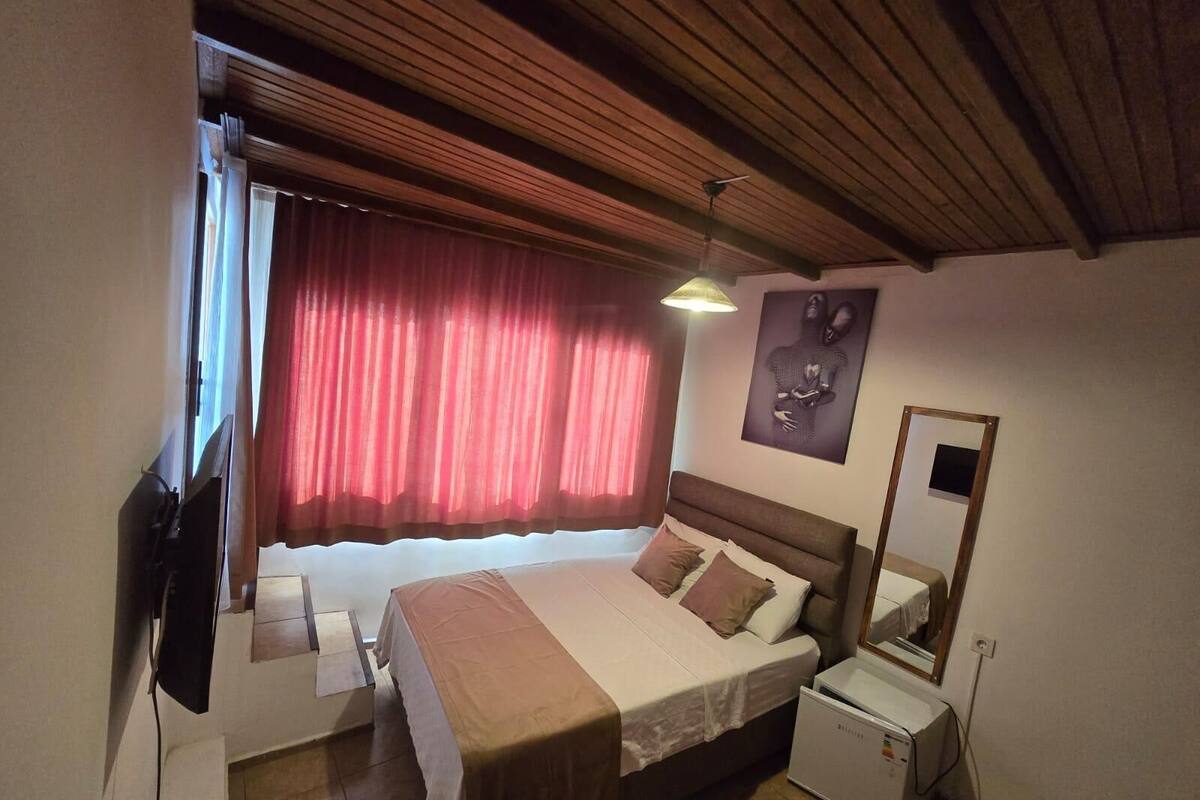 A bedroom with a bed, a nightstand, a television, a ceiling fan, and a window with curtains.