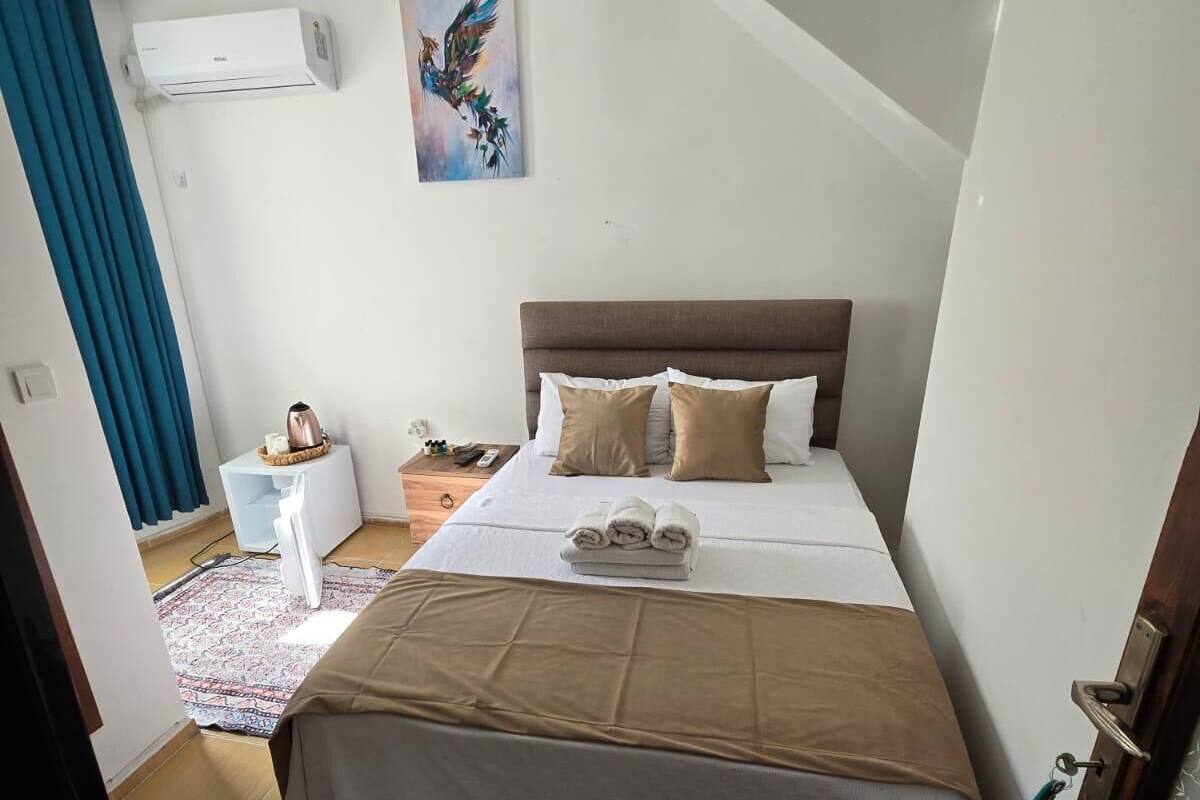 A bedroom with a bed, a bedside table, a nightstand, a wall-mounted air conditioner, a painting, and a patterned rug.