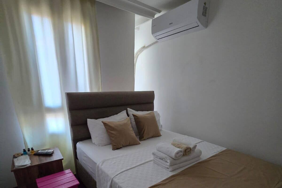 A hotel room with a bed, a small table, a pink stool, and a patterned rug.