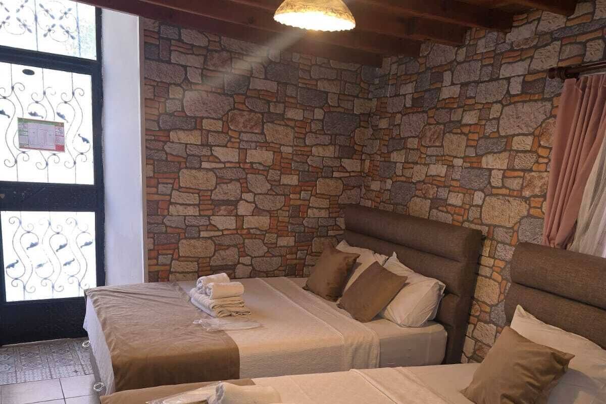 A room with two beds, a stone wall, a wooden ceiling, and a window with decorative ironwork.