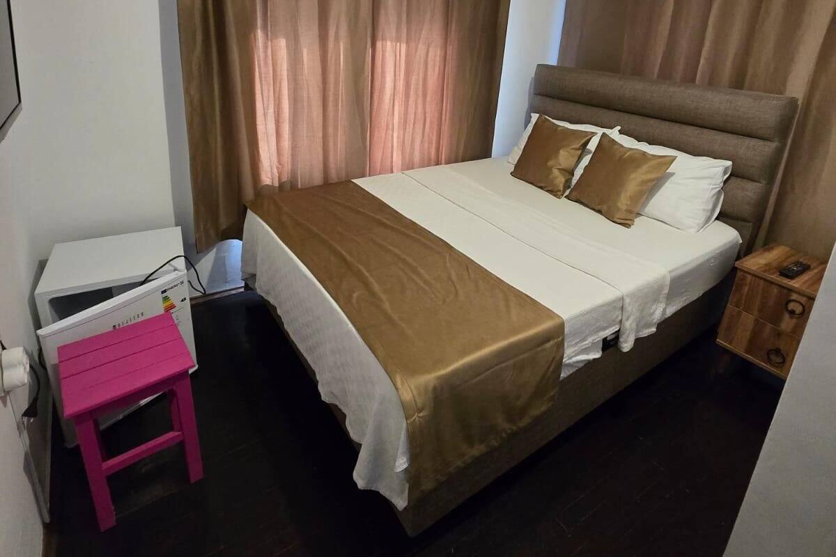 A bedroom with a bed, curtains, a nightstand, and a small pink table.