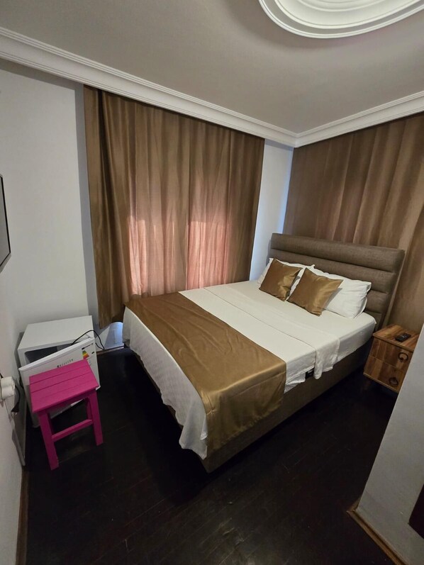 A bedroom with a bed, curtains, a nightstand, and a small pink table. - QMEYDANN (Ayvalik)