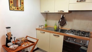 Une cuisine compacte équipée d’une cuisinière à gaz, d’un four et d’un petit évier. On y trouve une table en bois avec des aliments pour le petit-déjeuner et une machine à café.