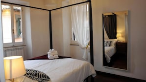 Un lit à baldaquin avec du linge de lit blanc, une lampe de chevet et un miroir qui reflète la pièce.