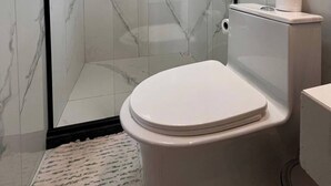 A modern bathroom with a glass-enclosed shower, a toilet, and marble walls. - Suite with air conditioning in Praia Seca - Araruama. (Araruama)