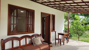 A wooden bench with cushions and a table, a wooden door, and a view of greenery outside. - Suite with air conditioning in Praia Seca - Araruama. (Araruama)