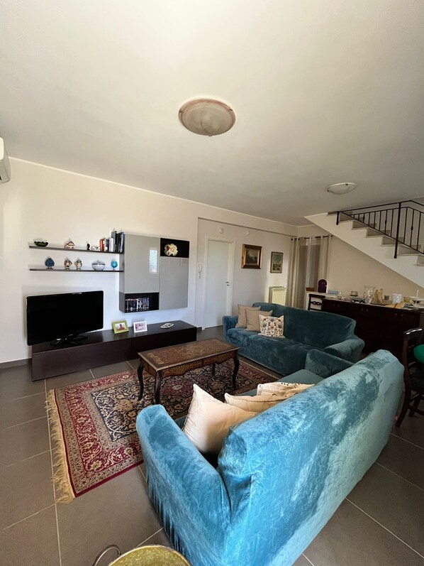 Ein Wohnzimmer mit Fernseher, Sofa, Couchtisch und einer Treppe.