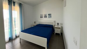 A bedroom with a bed, two bedside tables, a radiator, and a window with curtains.