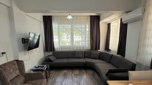 En moderne stue med en hjørnesofa, et træsofabord, en brun lænestol og et fladskærms-tv monteret på væggen.