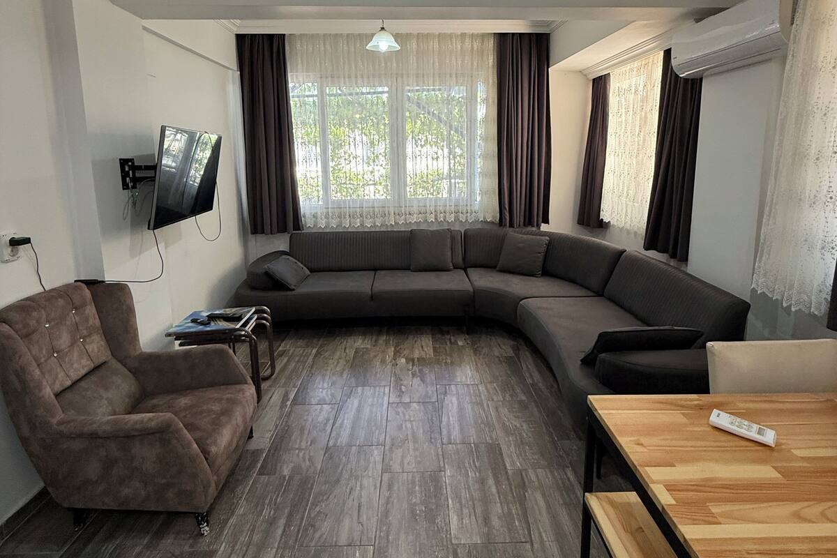 A modern living room with a sectional sofa, a wooden coffee table, a brown armchair, and a flat-screen TV mounted on the wall.