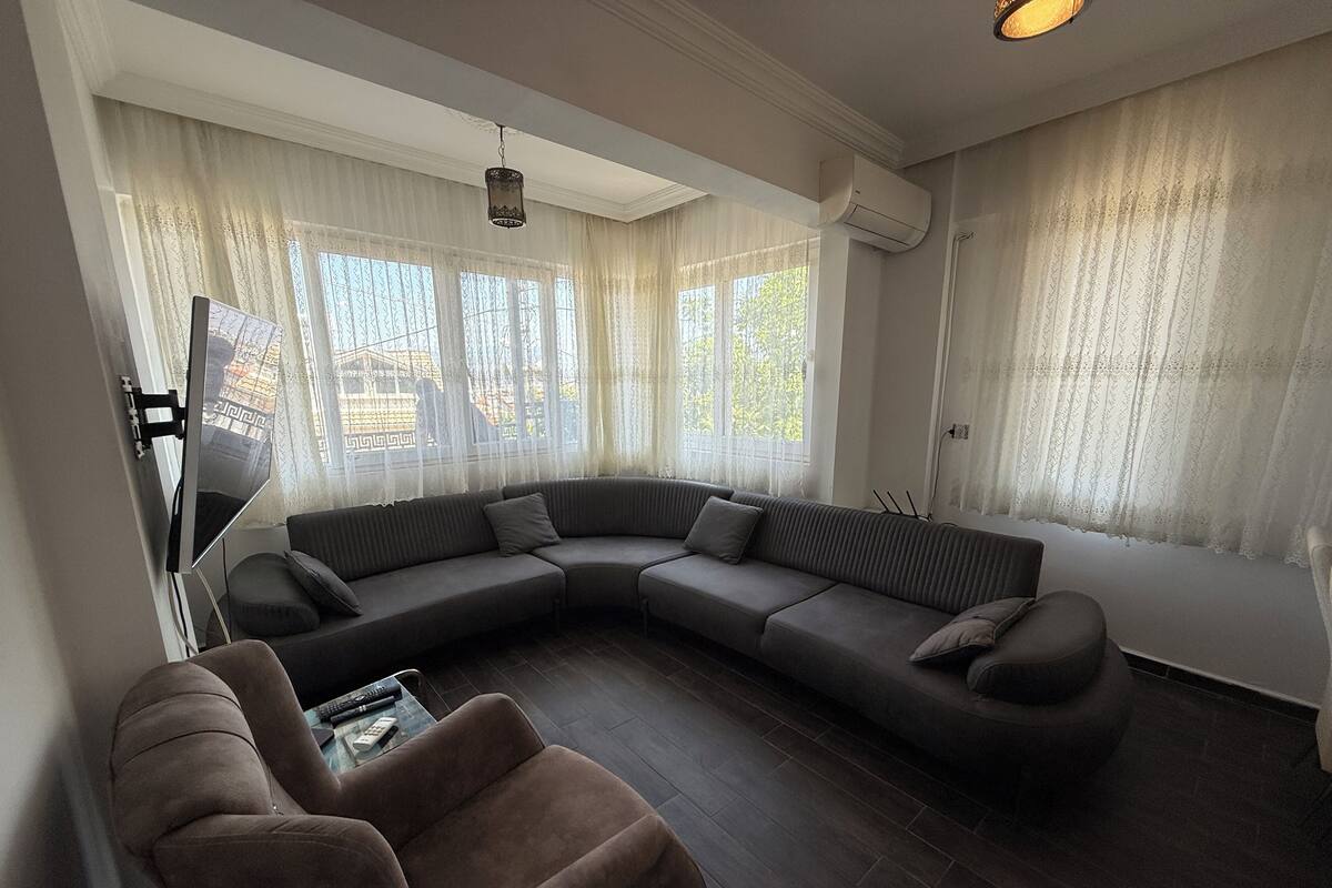 A modern living room with a sectional sofa, a brown armchair, and a flat-screen TV mounted on the wall.