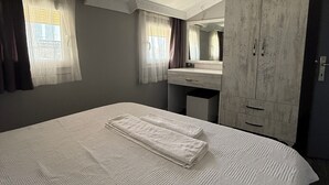 Et hotelværelse med en stor seng, et garderobeskab, et toiletbord med spejl og et vindue med gardiner.