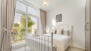 A bedroom with a bed, curtains, a window, a lamp, and a picture on the wall. - Community and Pool View 3BR Townhouse, Minutes from Desert Camp,DAMAC Hills 2 (Dubai)