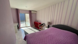 A bedroom with a large bed, a desk, a chair, and a window with curtains.