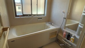 A bathroom with a bathtub, a window, a shower, and a mirror.