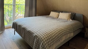 Ein Schlafzimmer mit einem großen Bett, Holzboden, schrägen Wänden und Blick durch ein Fenster.