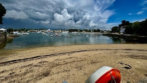 Eine Küstenlandschaft mit Sandstrand, einem ruhigen Hafen mit Booten und bewölktem Himmel.