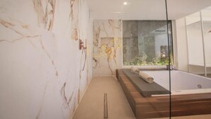 Een moderne badkamer met marmeren wanden, een glazen douchecabine en een houten bankje.