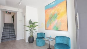 Un interior moderno con una escalera, dos sillones de terciopelo azul, una mesa con una revista y un cuadro abstracto grande.