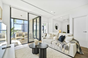 A modern living room with a sofa, coffee table, and a view of the city through large windows.