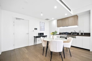 A modern kitchen with white cabinetry, a dining area with a round table and four chairs, and a small side table with a plant.