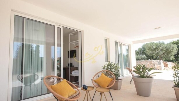 A balcony with wicker chairs and potted plants, large sliding glass doors, and a view of the outdoors.