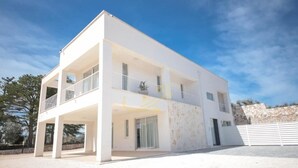 A modern two-story building with a flat roof, large windows, and a covered outdoor area with a balcony.