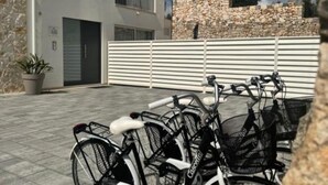 A row of bicycles parked in front of a building with a stone wall and a white fence.