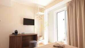 A modern hotel room with a bed, a desk, a television, and a wardrobe.