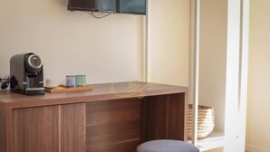 A modern room with a wooden desk, a coffee maker, and a television mounted on the wall.