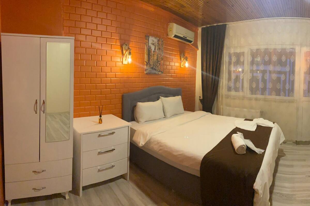 Une chambre à coucher comprenant un lit, une armoire, une table de chevet, un appareil de climatisation et une fenêtre avec des rideaux.