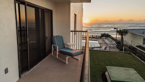 A balcony with a view of the ocean at sunset, a chair, and a small table. - Ocean Delight 2/2 Sandpoint Condo Great OceanViews Pool, Great Rates (Daytona Beach)