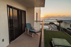 Un balcon avec vue sur l’océan au coucher du soleil, une chaise et une petite table.