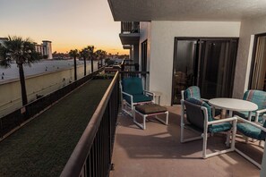 A balcony with a view of the sunset, a small grassy area, and outdoor furniture. - Ocean Delight 2/2 Sandpoint Condo Great OceanViews Pool, Great Rates (Daytona Beach)