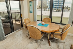 A conference room with a wooden table, four chairs, and a view of the beach through large windows. - Ocean Delight 2/2 Sandpoint Condo Great OceanViews Pool, Great Rates (Daytona Beach)
