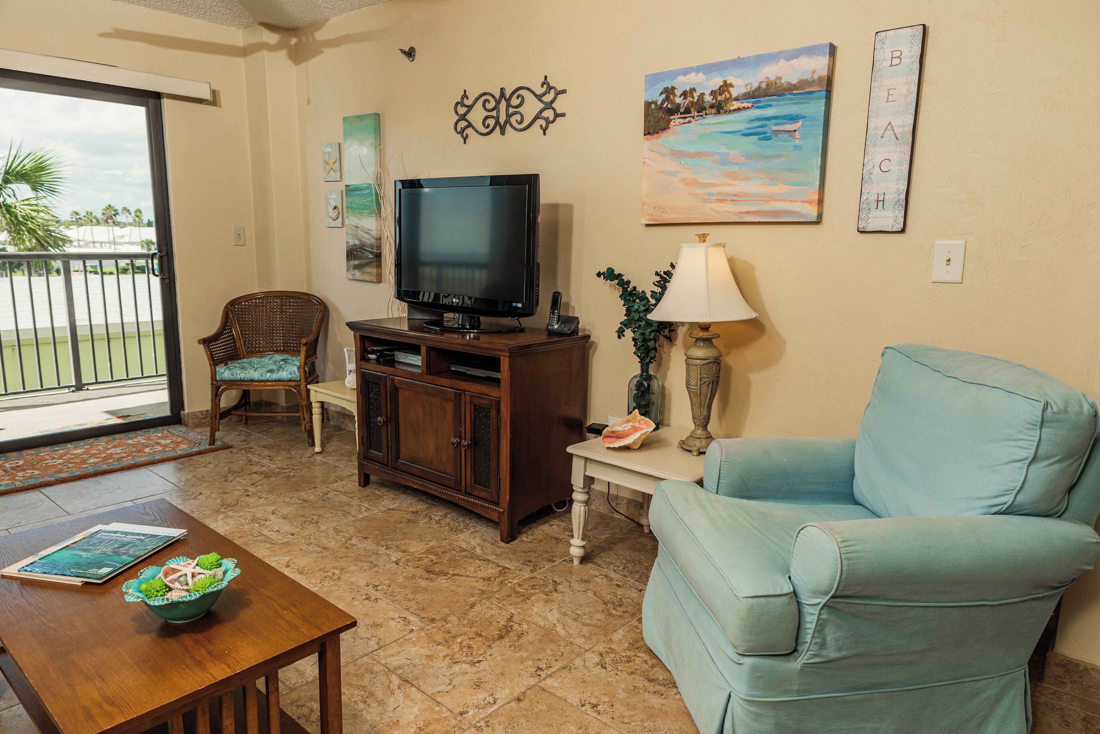 A living room with a television, a blue armchair, a wooden coffee table, and a dining chair.