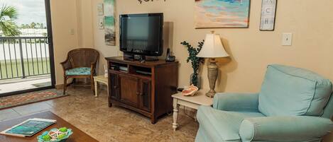 A living room with a television, a blue armchair, a wooden coffee table, and a dining chair.