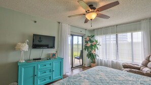 A bedroom with a bed, a ceiling fan, a TV, a dresser, and a window with a view of the outdoors. - Sunnyside Up, 1st FL 2 BR Beach Condo, Oceanfront Pool, Sandpoint 1E (Daytona Beach)