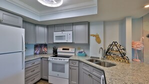 A kitchen with grey cabinets, a white refrigerator, a microwave, a stove, and a sink. - Sunnyside Up, 1st FL 2 BR Beach Condo, Oceanfront Pool, Sandpoint 1E (Daytona Beach)