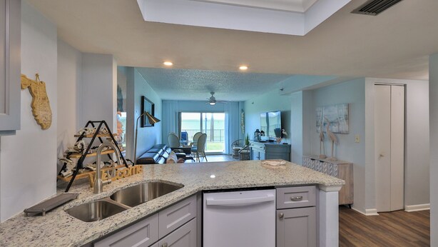 A modern kitchen with a double sink, white cabinets, and a granite countertop. - Sunnyside Up, 1st FL 2 BR Beach Condo, Oceanfront Pool, Sandpoint 1E (Daytona Beach)