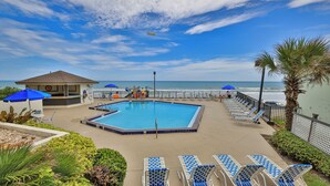 A pool area with lounge chairs and umbrellas, a lifeguard tower, and a view of the ocean. - Sunnyside Up, 1st FL 2 BR Beach Condo, Oceanfront Pool, Sandpoint 1E (Daytona Beach)