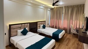 A hotel room with two beds, a desk, a TV, and a ceiling fan. - Hotel Navil Exotica (Vasco da Gama)