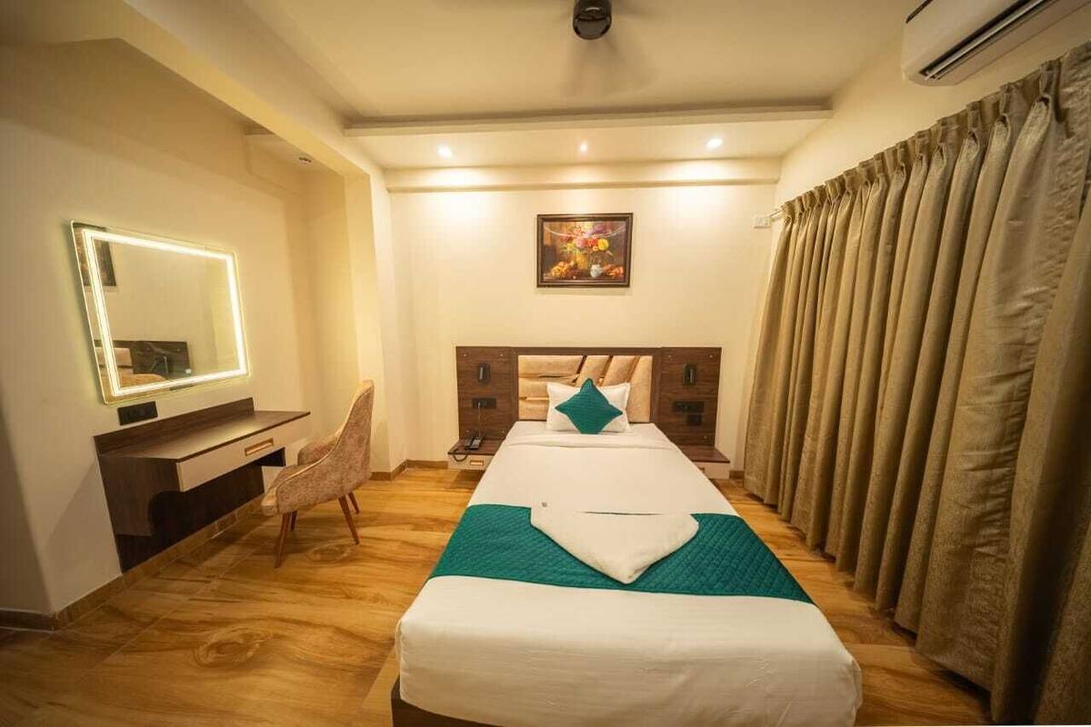 Un cuarto de hotel con una cama, un escritorio con espejo, una silla, una mesita de noche y un cuadro en la pared.