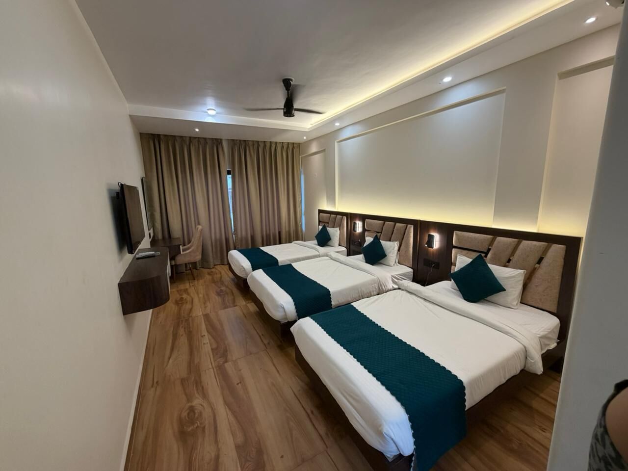 A hotel room with two beds, a flat-screen TV, a ceiling fan, and a wooden floor.