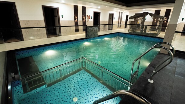 A swimming pool with clear blue tiles, a glass barrier, and a metal handrail. - Hotel Navil Exotica (Vasco da Gama)