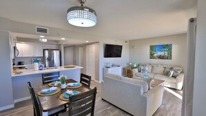 A modern kitchen with white cabinets, a stainless steel refrigerator, and a dining area with a wooden table and chairs. - Coastal Charm, 1stFL Stunning Oceanfront 2BR Condo, Lg Balcony, Pool (Daytona Beach)